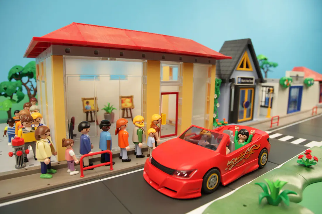 Playmobil people queuing for a gallery while a red sports car passes